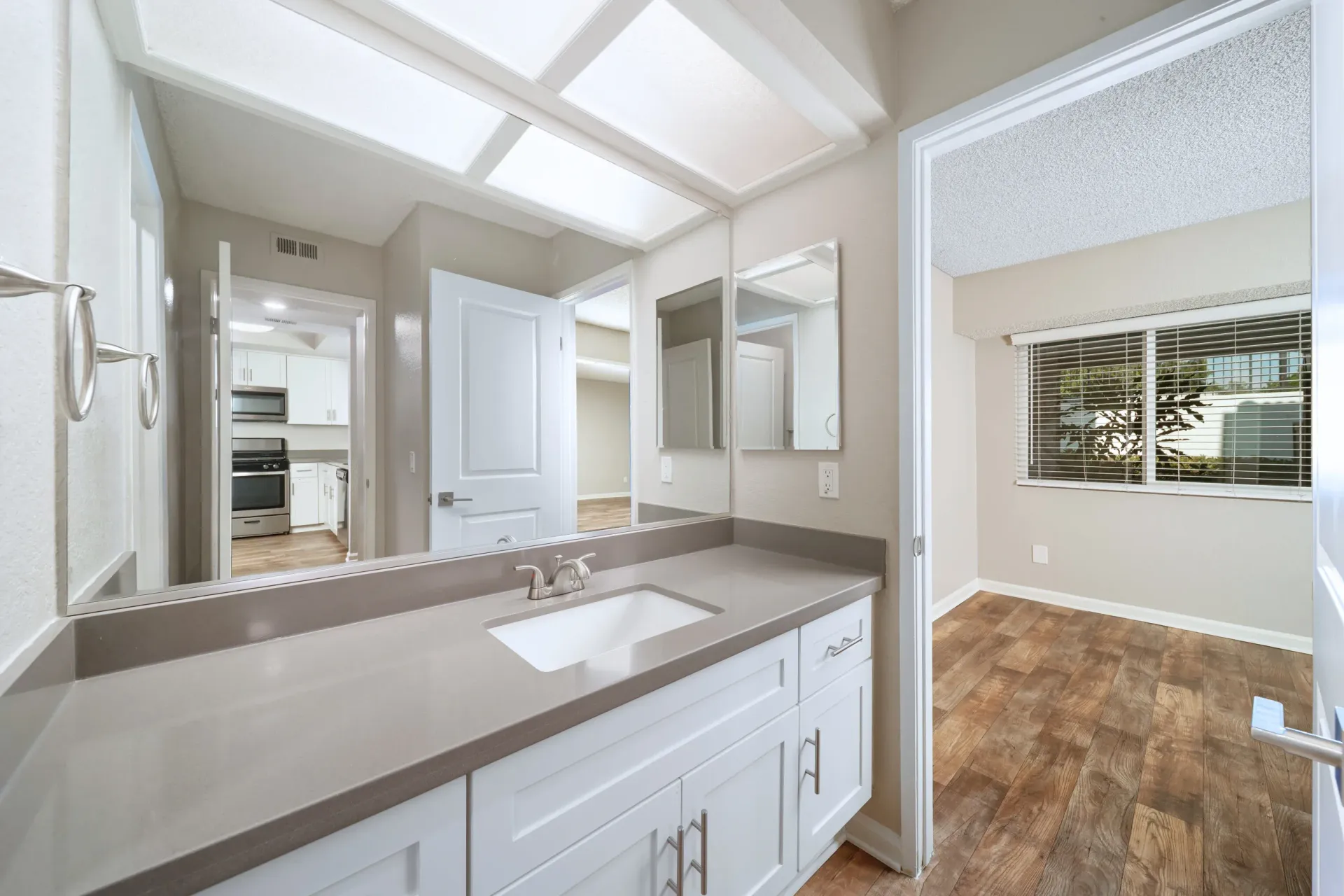 Bathroom vanity with sink and large mirror; doorway to kitchen visible at Sonora at Alta Loma apartments in Alta Loma, CA.