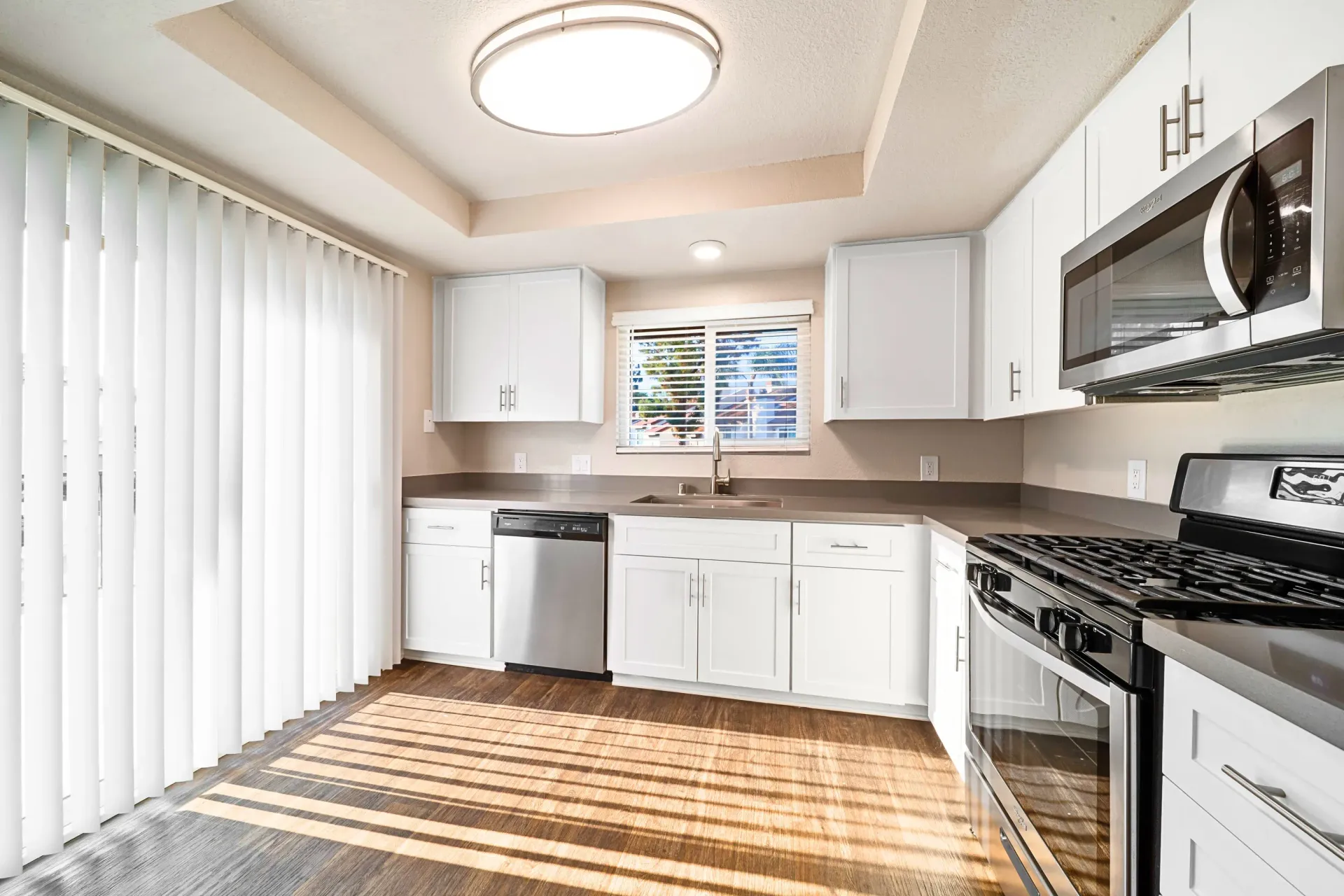 Bright white kitchen in an apartment with stainless steel appliances and window blinds at Sonora at Alta Loma apartments in Alta Loma, CA.