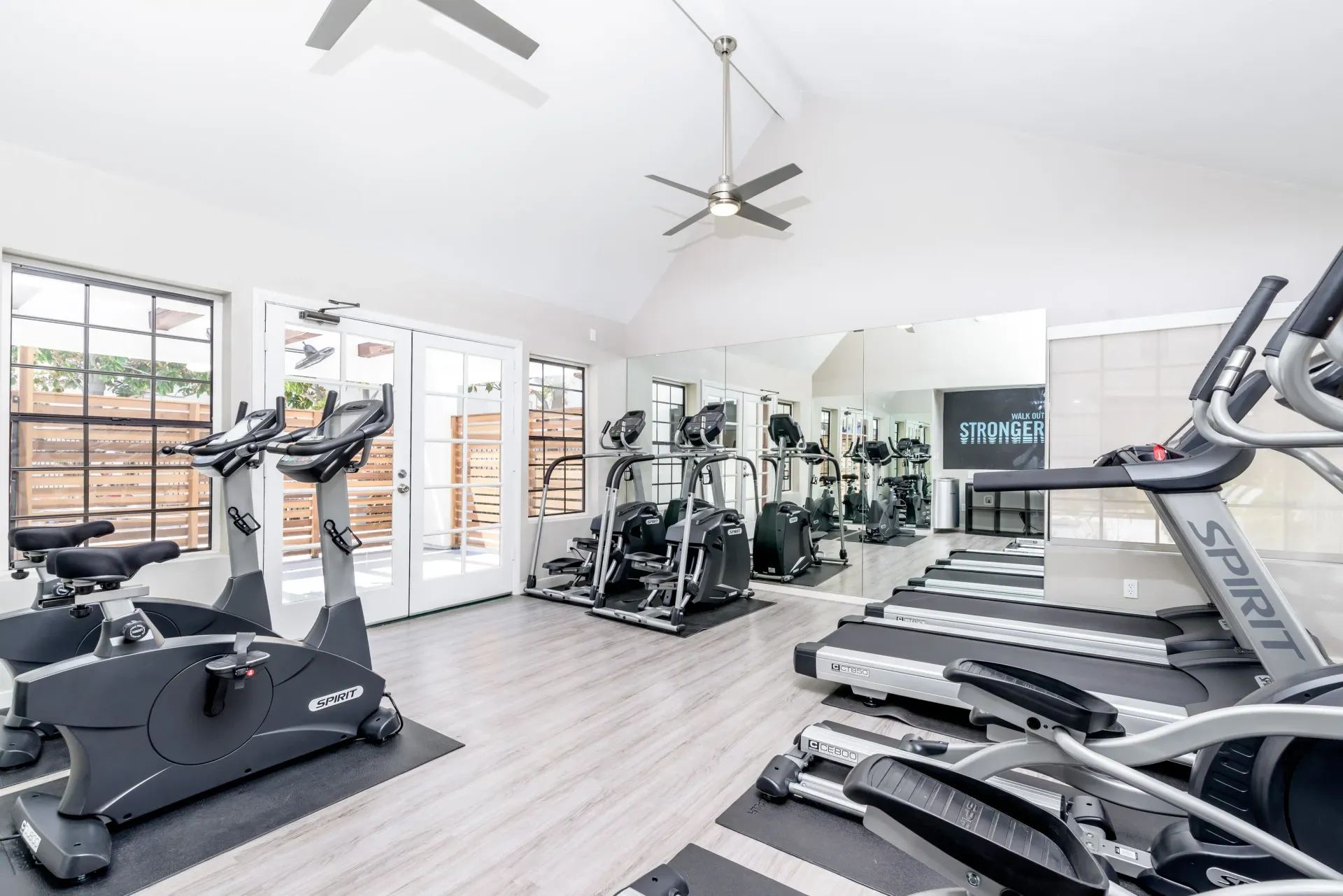 Well-equipped indoor community gym with treadmills and stationary bikes, mirrors, and windows at Sonora at Alta Loma apartments in Alta Loma, CA.