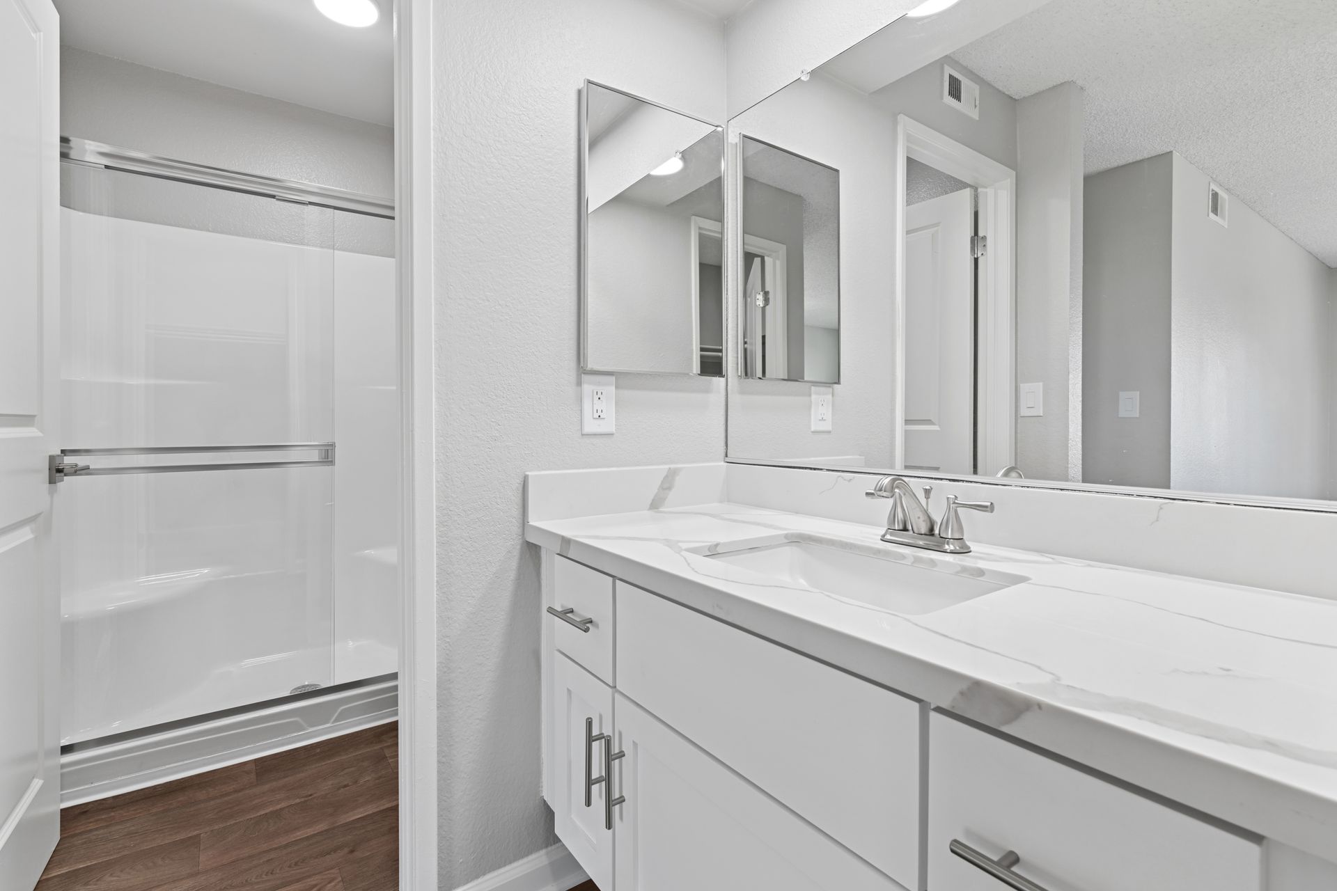 Bright white bathroom with vanity, mirror, and walk-in shower