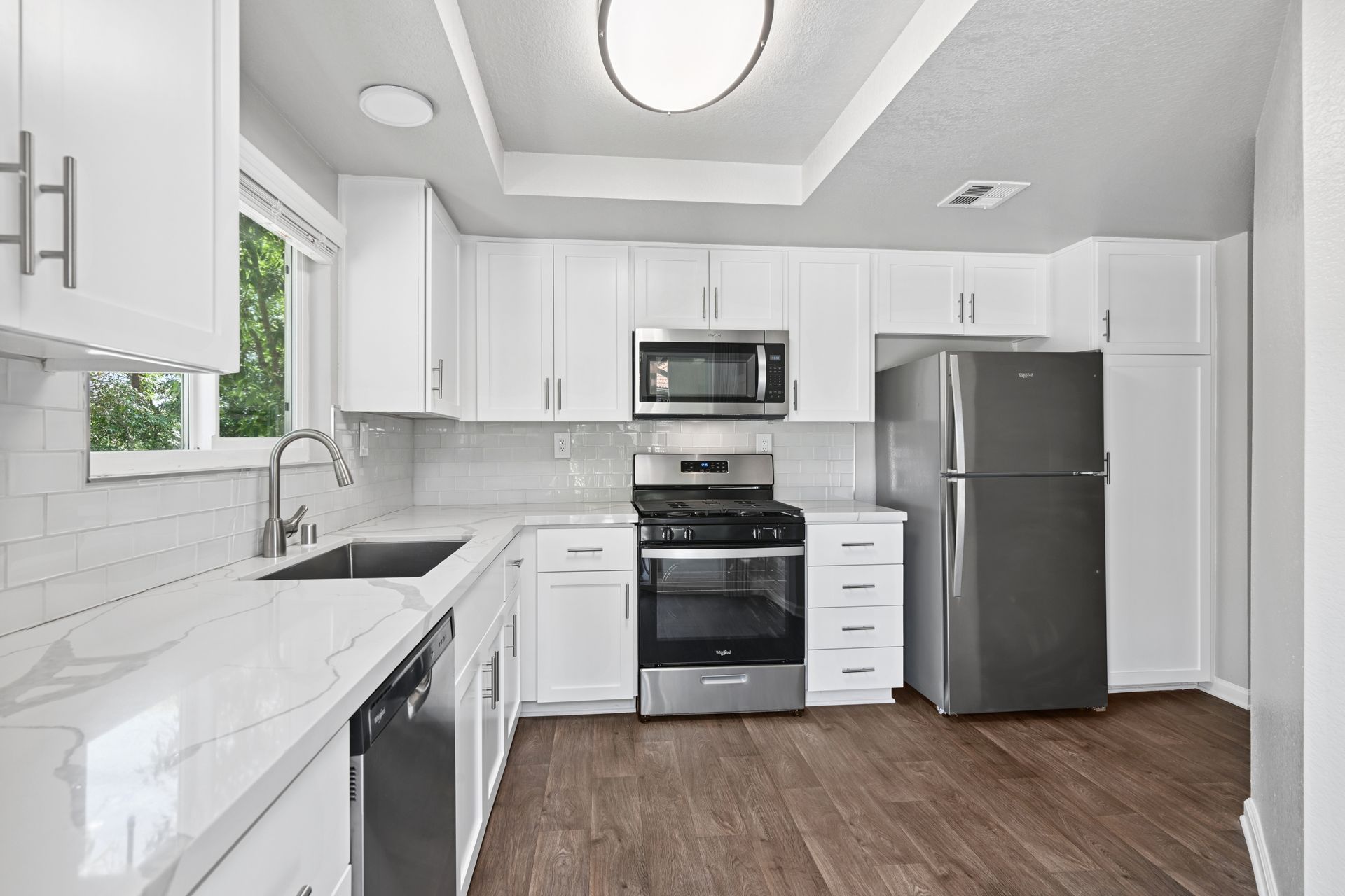 Bright white kitchen with stainless steel appliances, white cabinets, and wood flooring