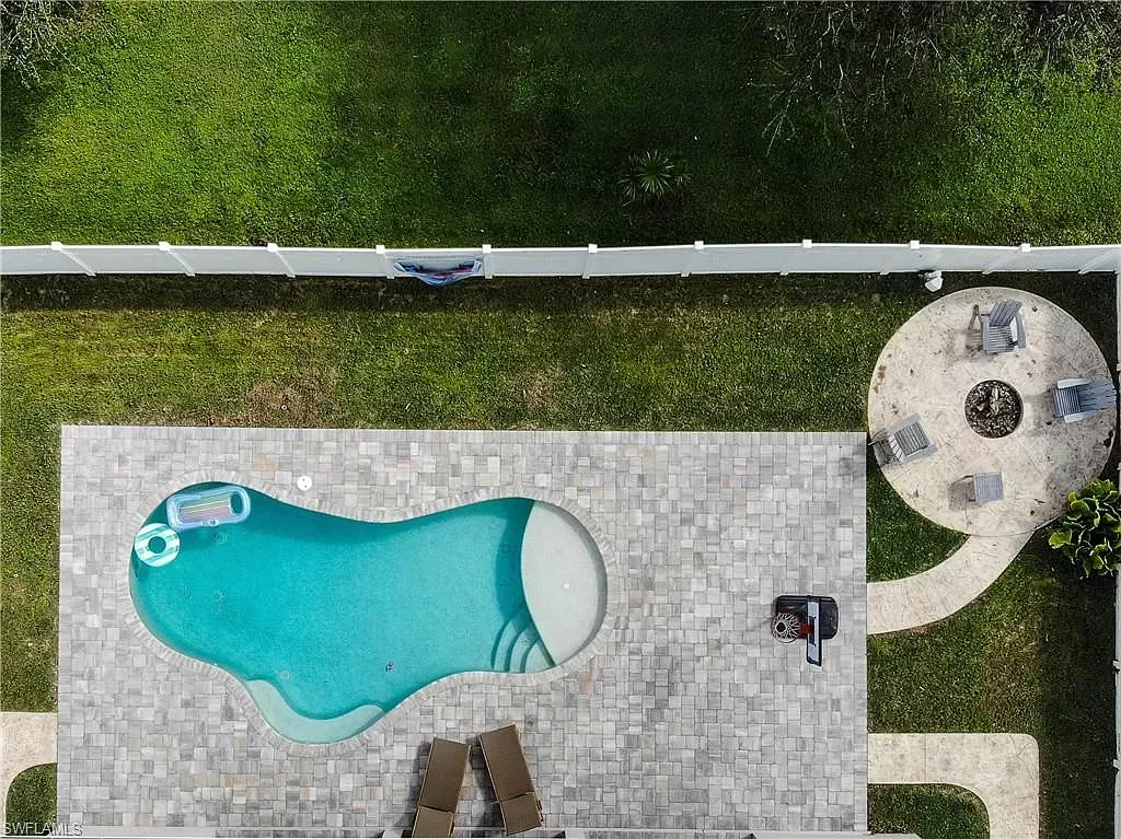 Overhead view of a pool, patio, and fire pit in a grassy backyard.