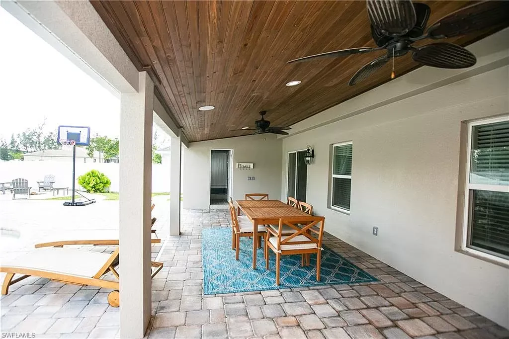 Covered patio with a dining table, chairs, and a rug; overlooking a pool area.