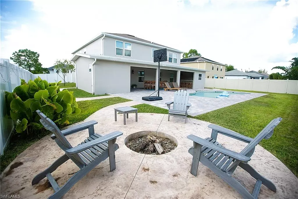Backyard with fire pit, Adirondack chairs, pool, and two-story house.