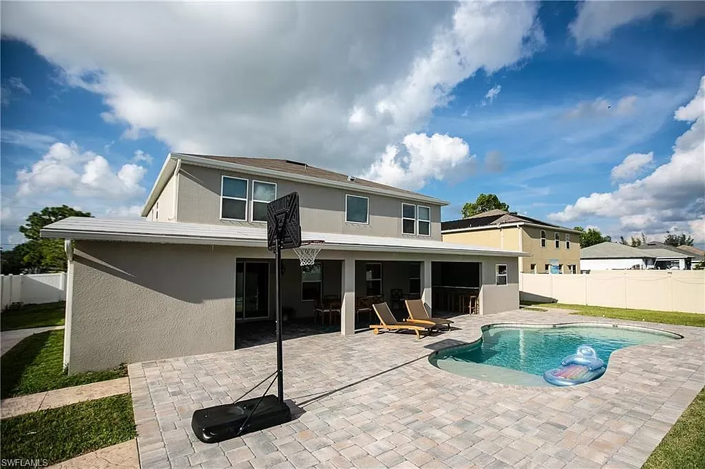 Backyard with pool, patio, house, basketball hoop, and blue sky.