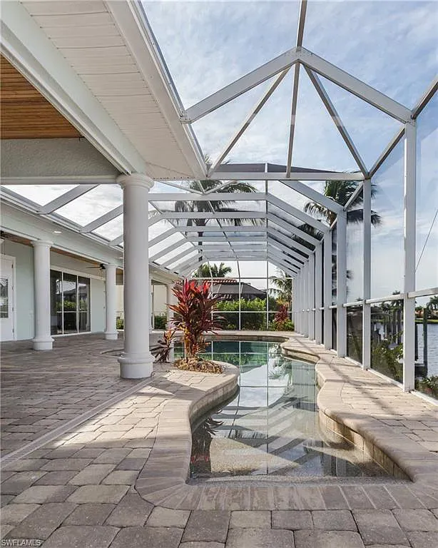 Patio with pool, enclosed by screened frame. Light brick floor, white columns, water, and greenery.