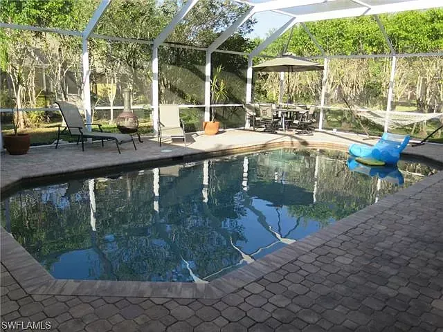 A backyard pool enclosed by a screen. There are lounge chairs and a table with chairs around the pool area.