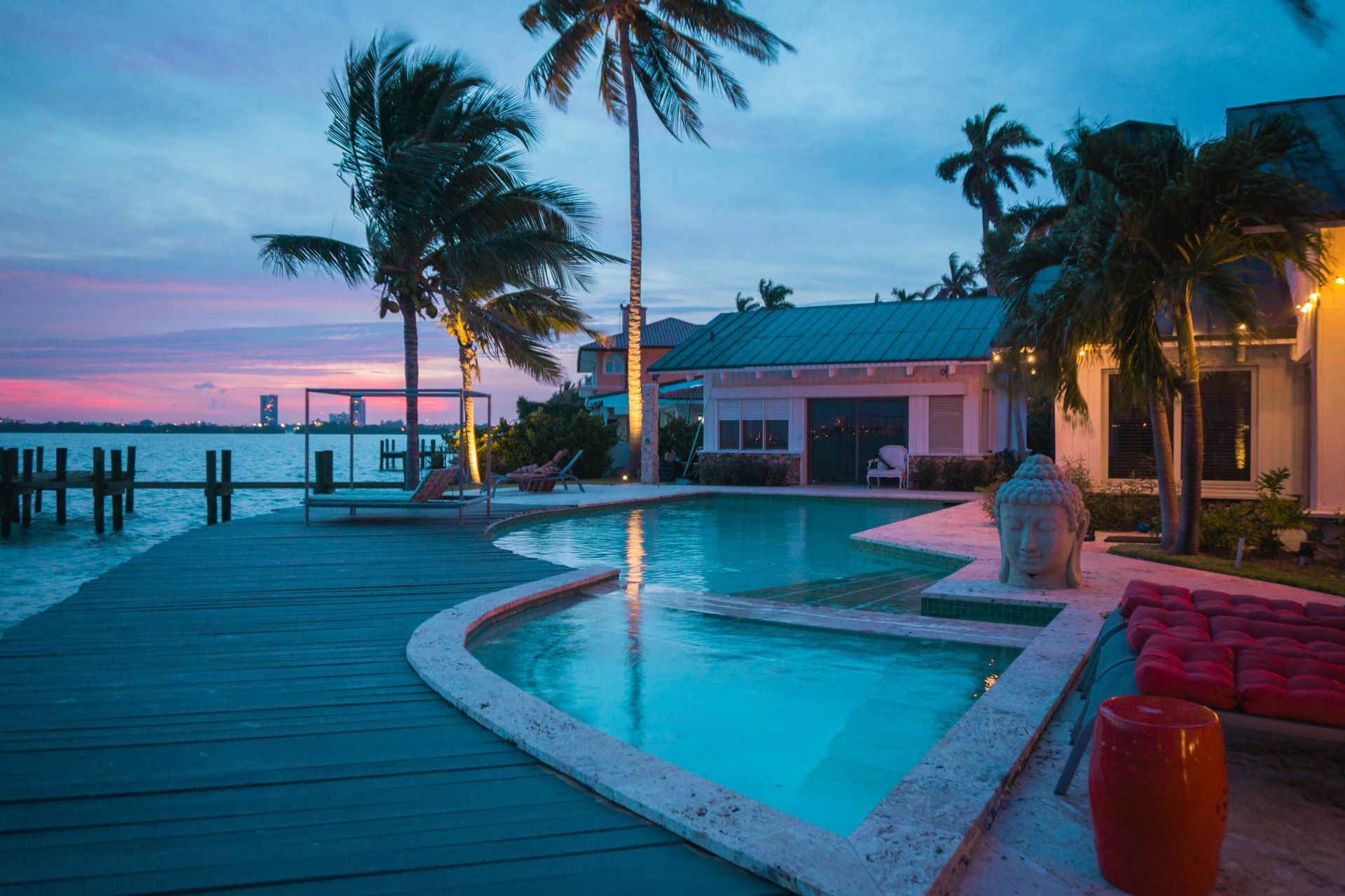 Poolside evening scene with palm trees, water, and a building, bathed in twilight colors.