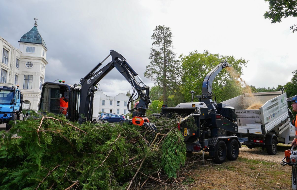 Excavators and a dump truck clearing storm debris near a white building in a grassy area