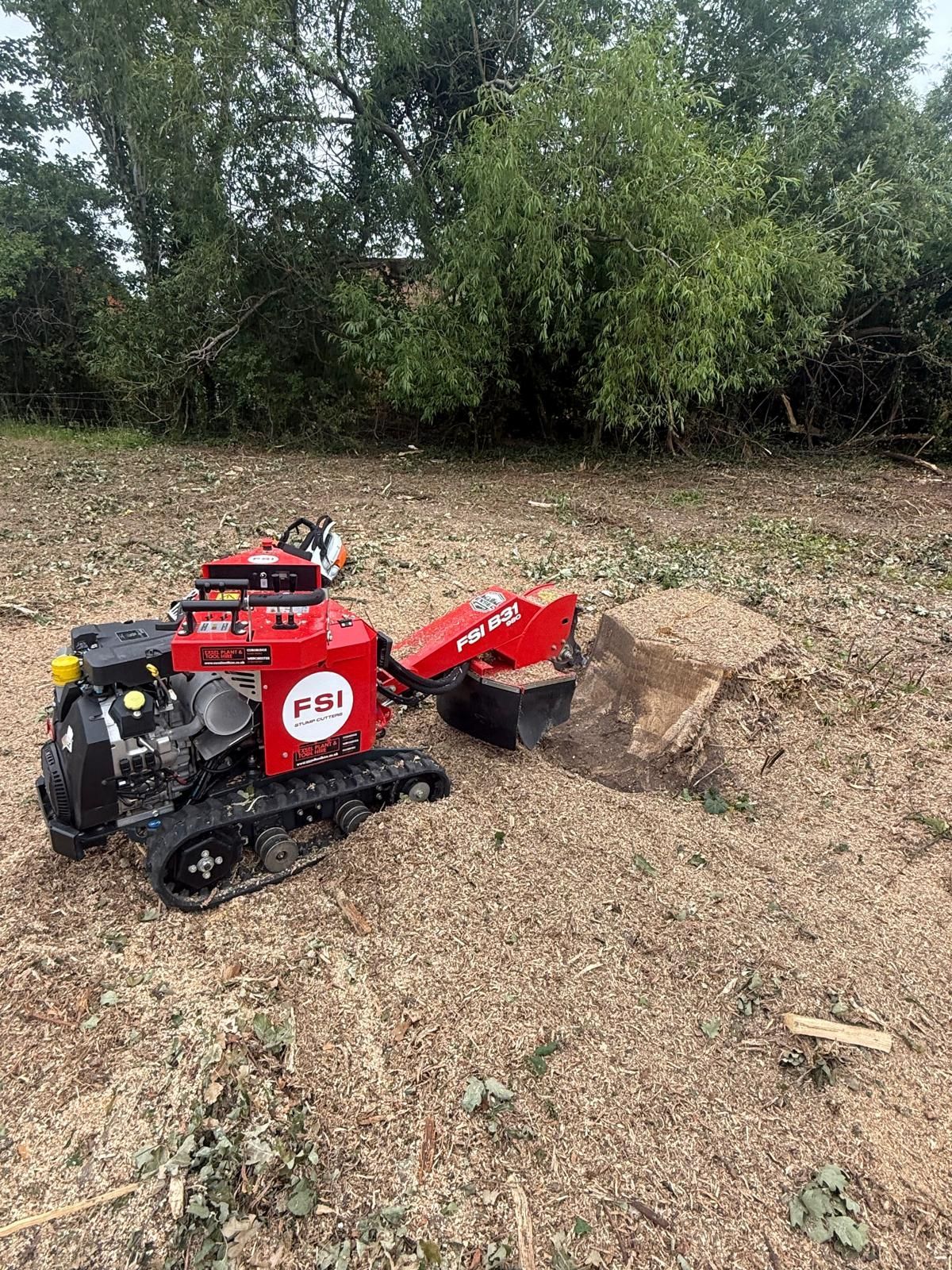 Red tracked mini excavator digging a mound of dirt in a dry field with trees in the background