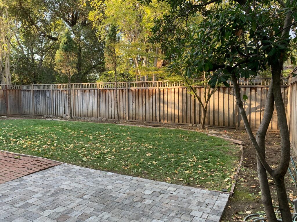 A backyard with a wooden fence and a brick patio.