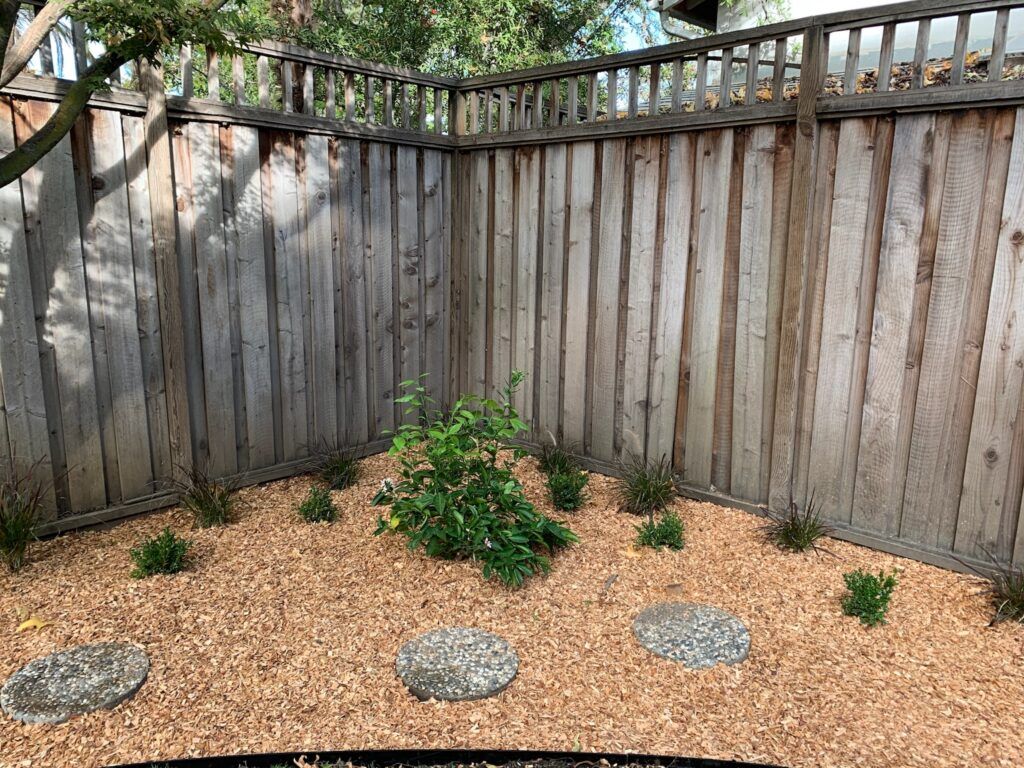 A wooden fence surrounds a garden with gravel and plants.