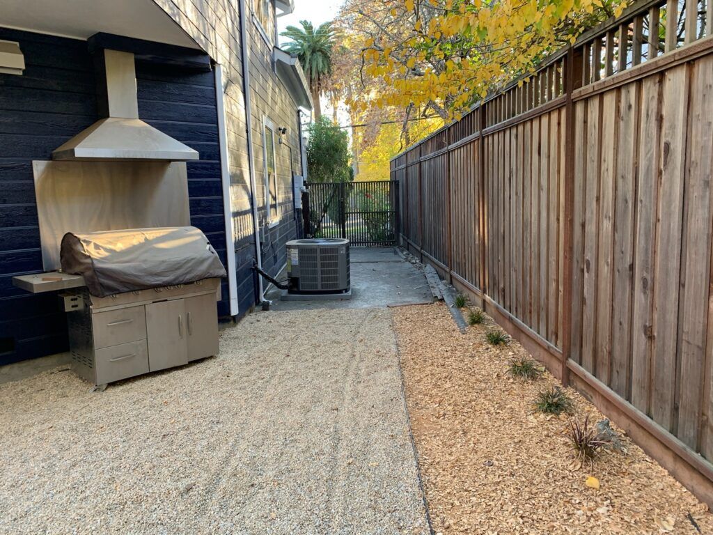 A backyard with a grill and a wooden fence.