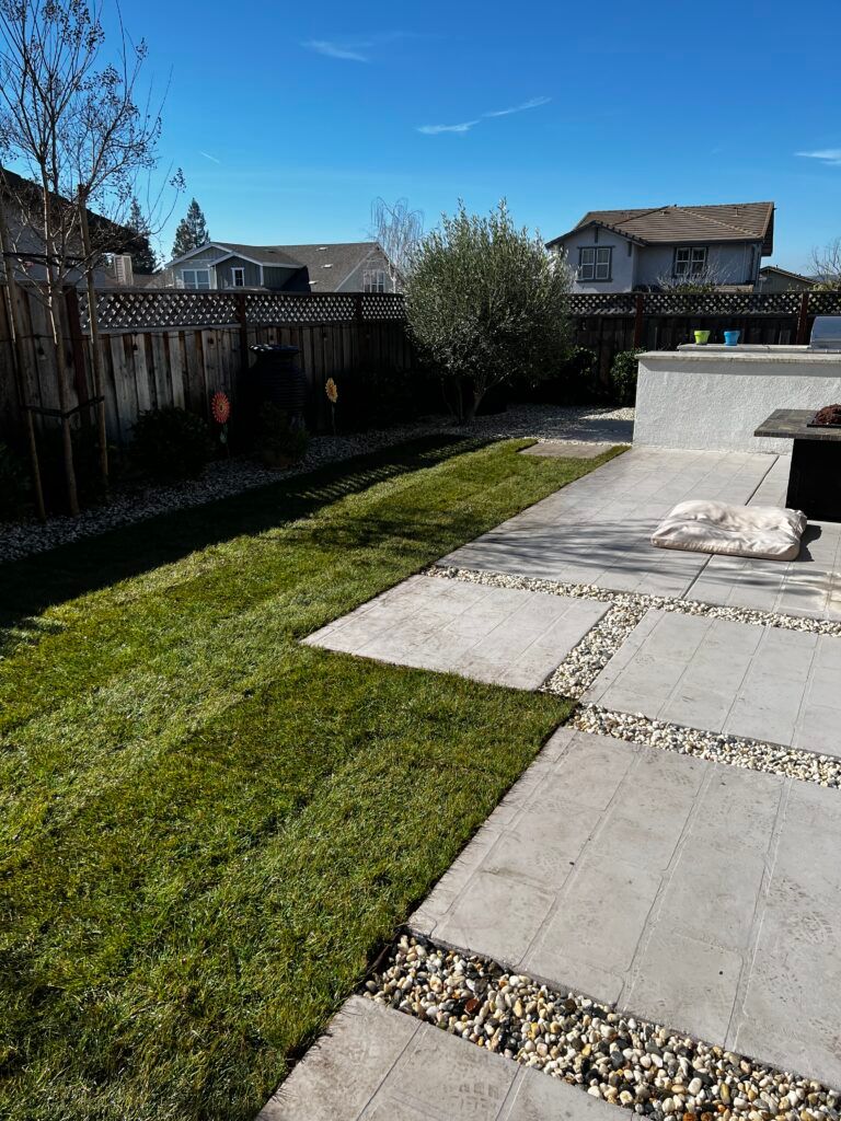 A lawn with a patio and a fence in the background.