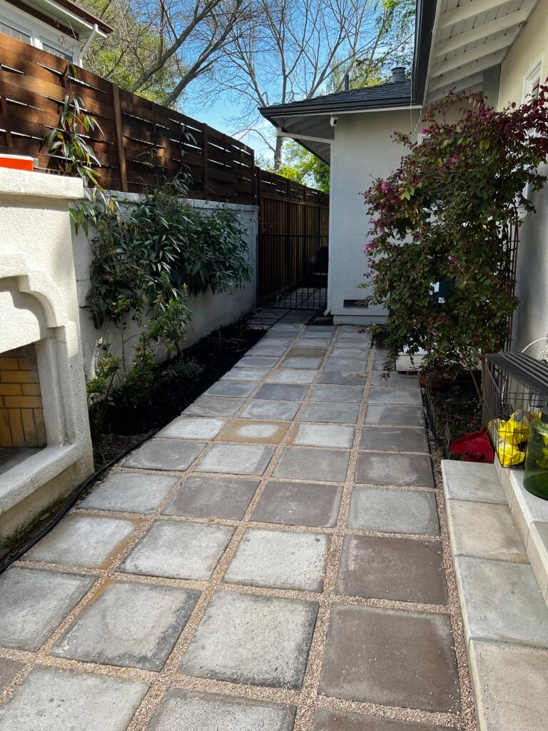 A walkway leading to a house with a fireplace in the backyard.