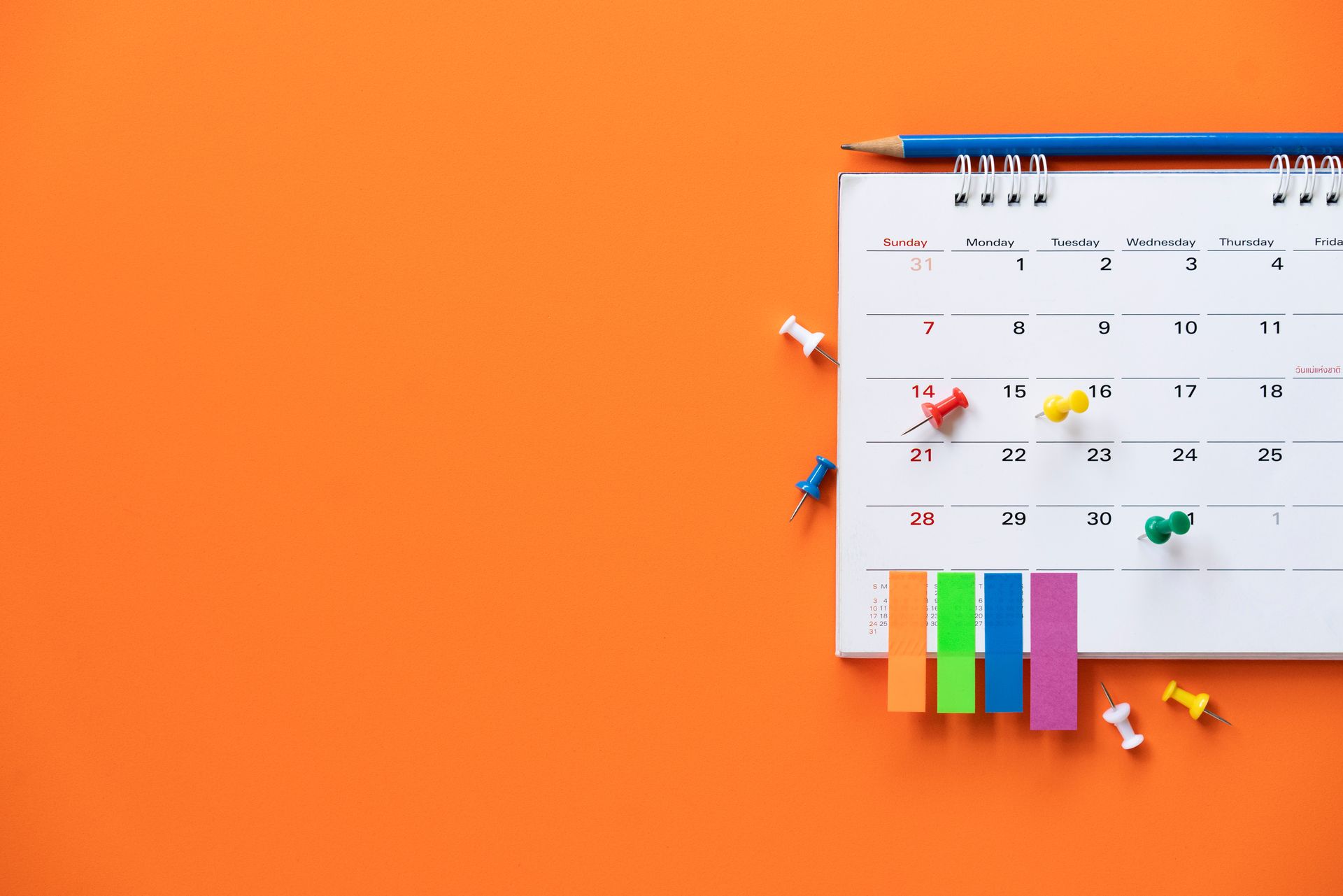 Calendar with pushpins and sticky notes on orange background. Pencil on top.