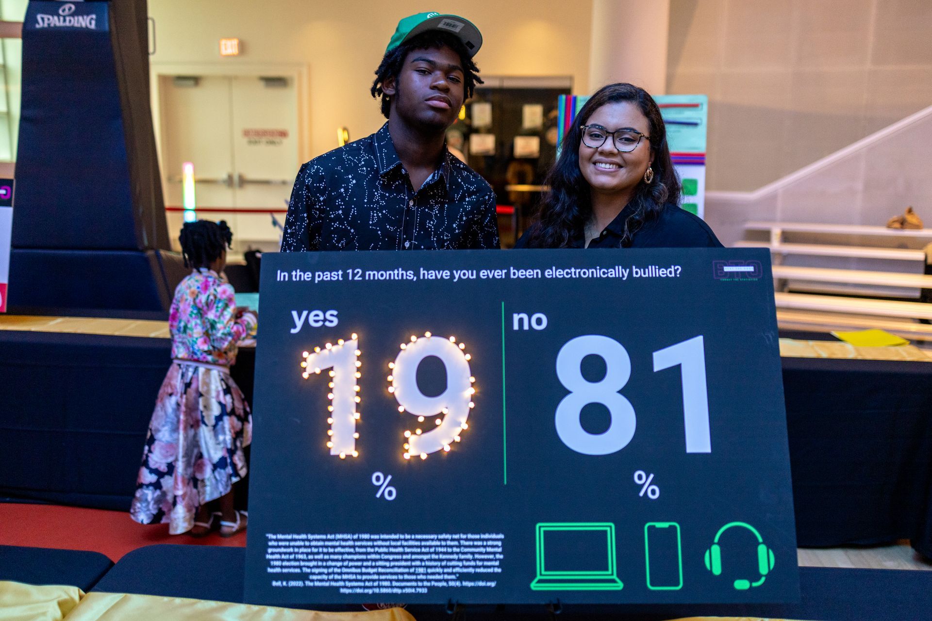 A youth and adult standing behind a project with facts on being eletronically bullied.