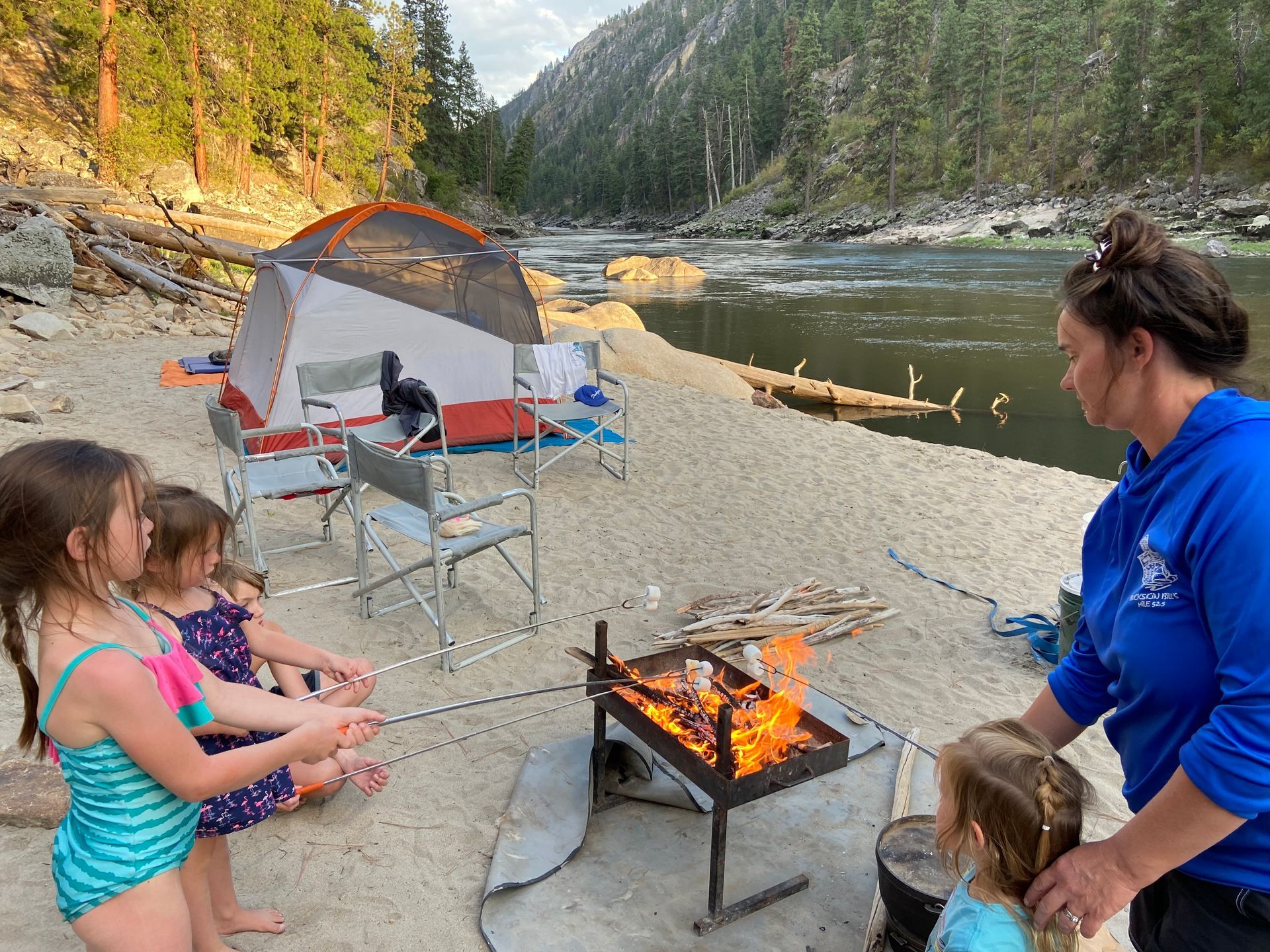 A woman and three little girls are roasting marshmallows over a campfire.