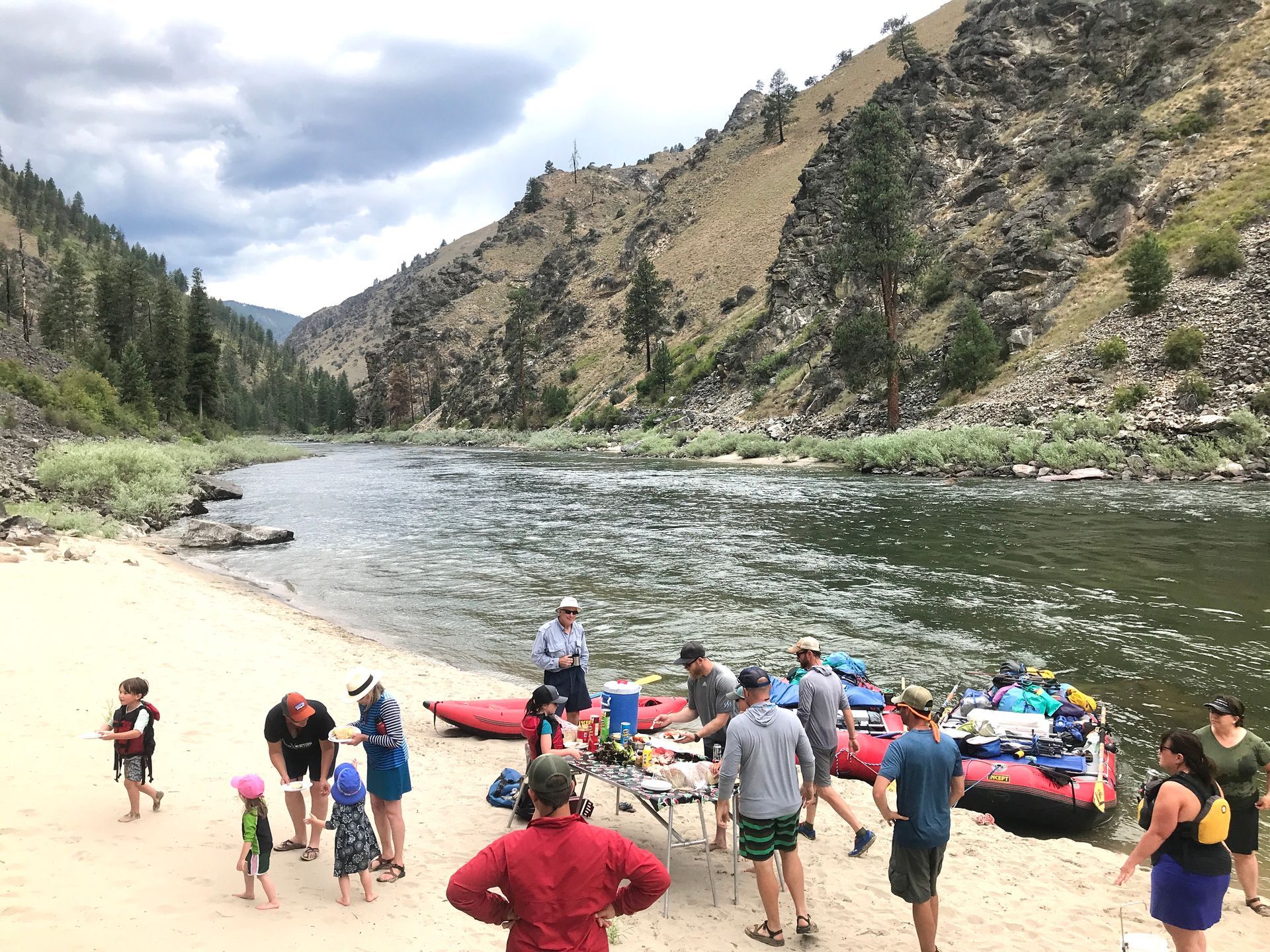 A group of people are standing on a beach next to a river.