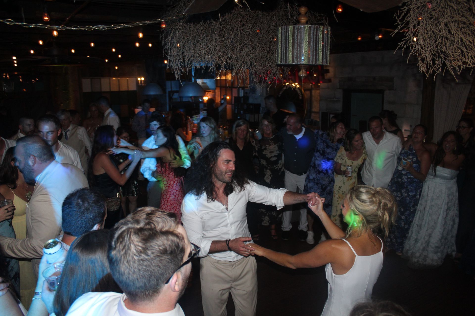 People dancing at a nighttime celebration, under string lights and organic decor.