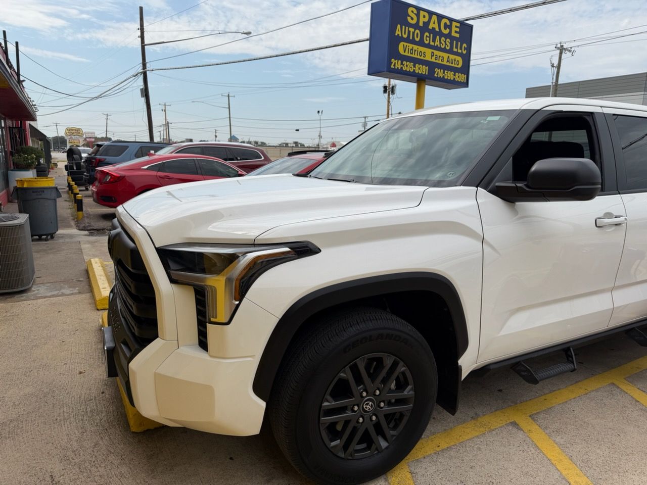 White pickup truck parked outside a small lot with other cars and a roadside sign in the background