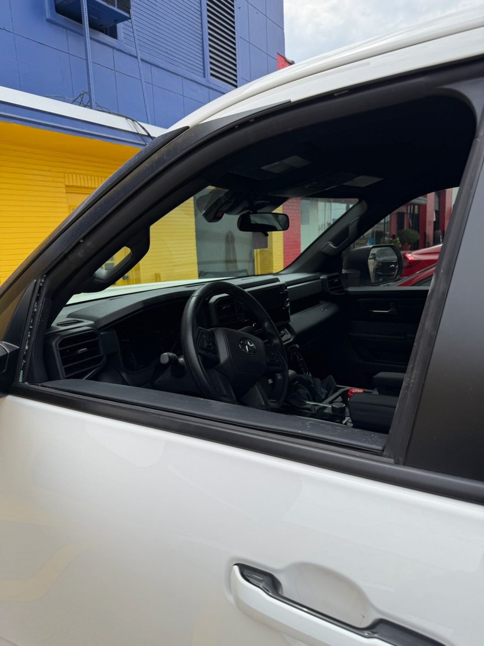 Car interior viewed through open window beside a yellow building and blue wall