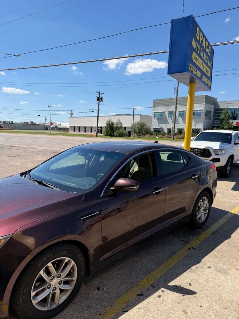 Maroon sedan parked by a roadside sign under a blue sky