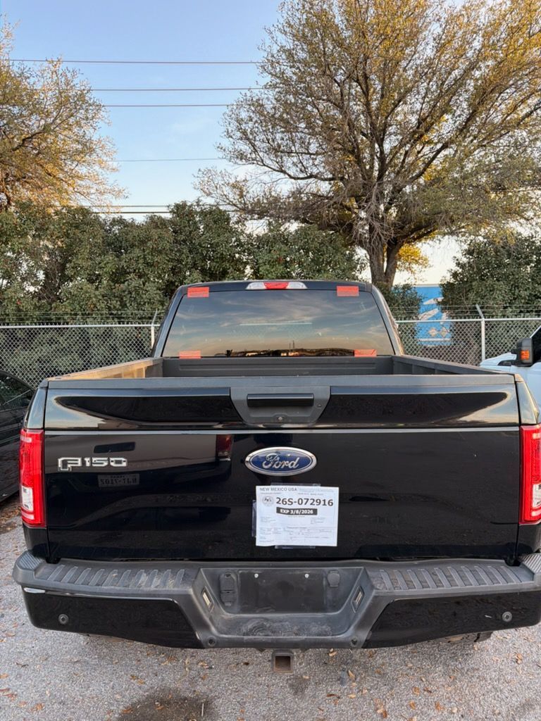 Black Ford F-150 pickup parked behind a chain-link fence with trees in the background