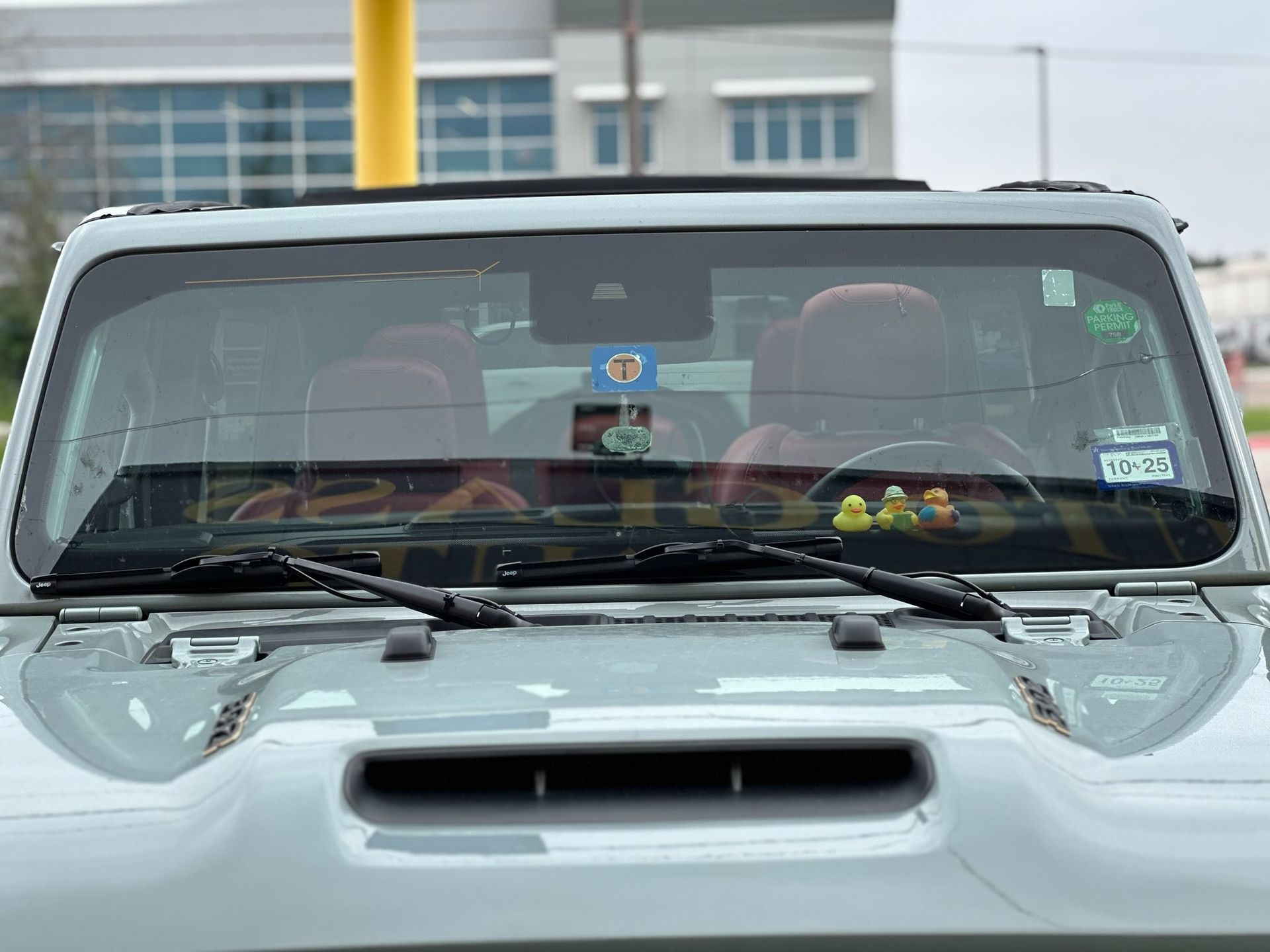 Front view of a light gray SUV with items on the dashboard, parked in front of a building