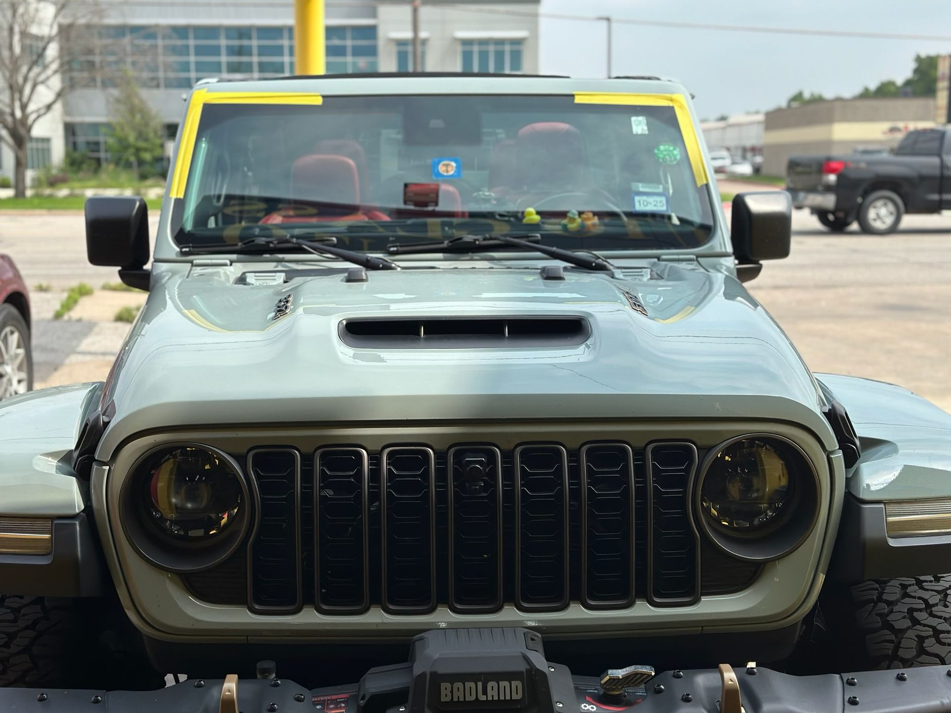 Front view of a green Jeep Wrangler with yellow roof trim parked outside a building.