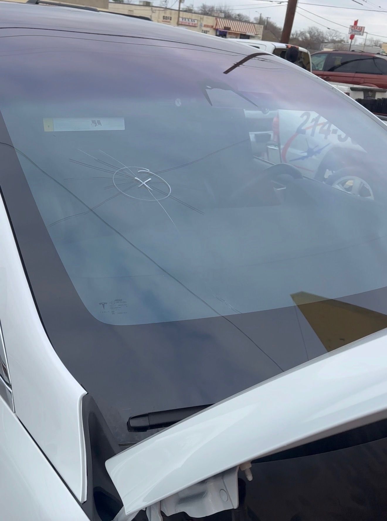 White car with a cracked windshield in a parking lot, with the hood raised.