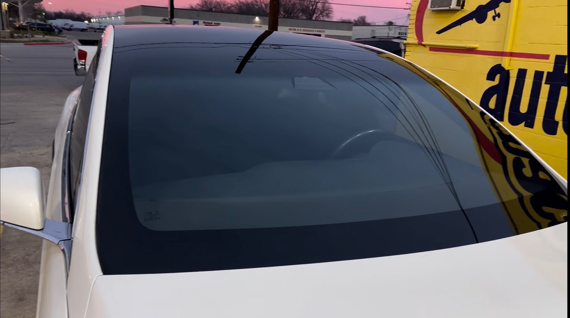 White car with dark tinted windshield parked beside a yellow truck at sunset