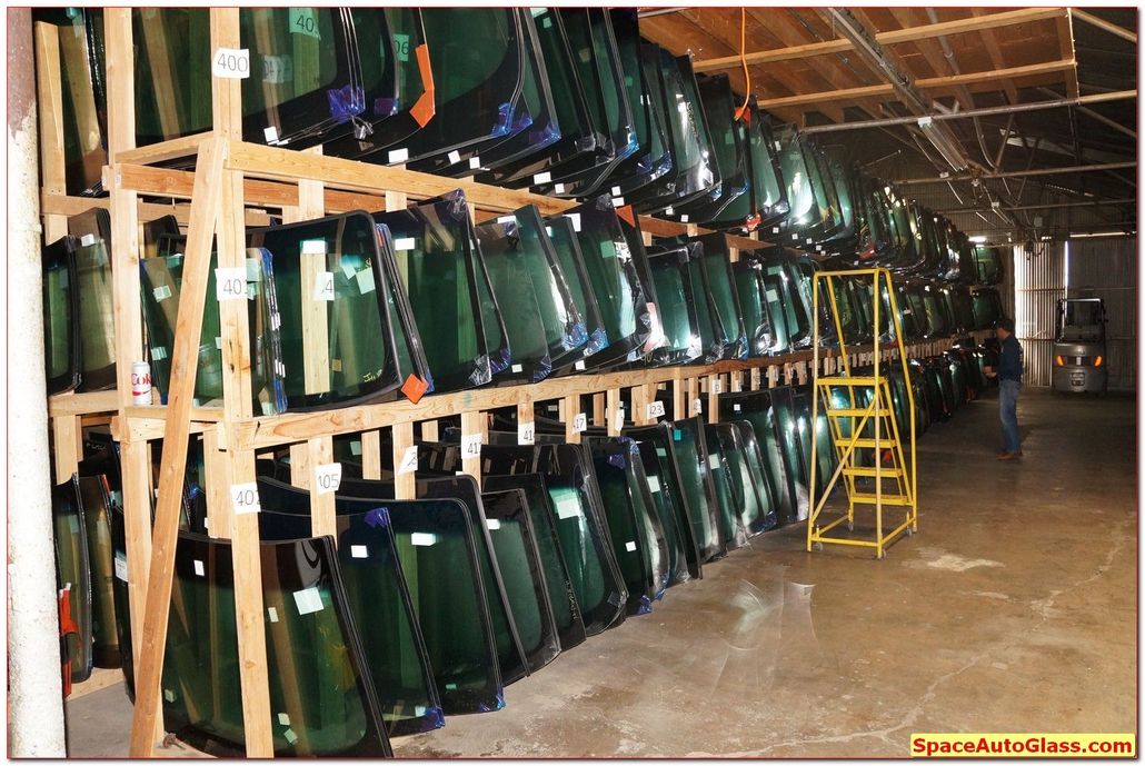 Rows of green glass panels stacked in a warehouse on metal racks, with a yellow ladder in front