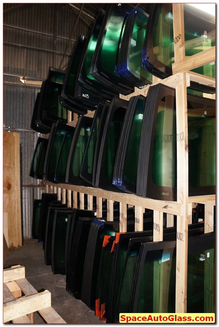 Stacked car windshields and glass panels stored on wooden racks in a warehouse.