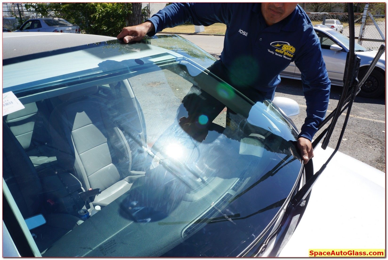 Person cleaning a white car windshield outdoors with a squeegee