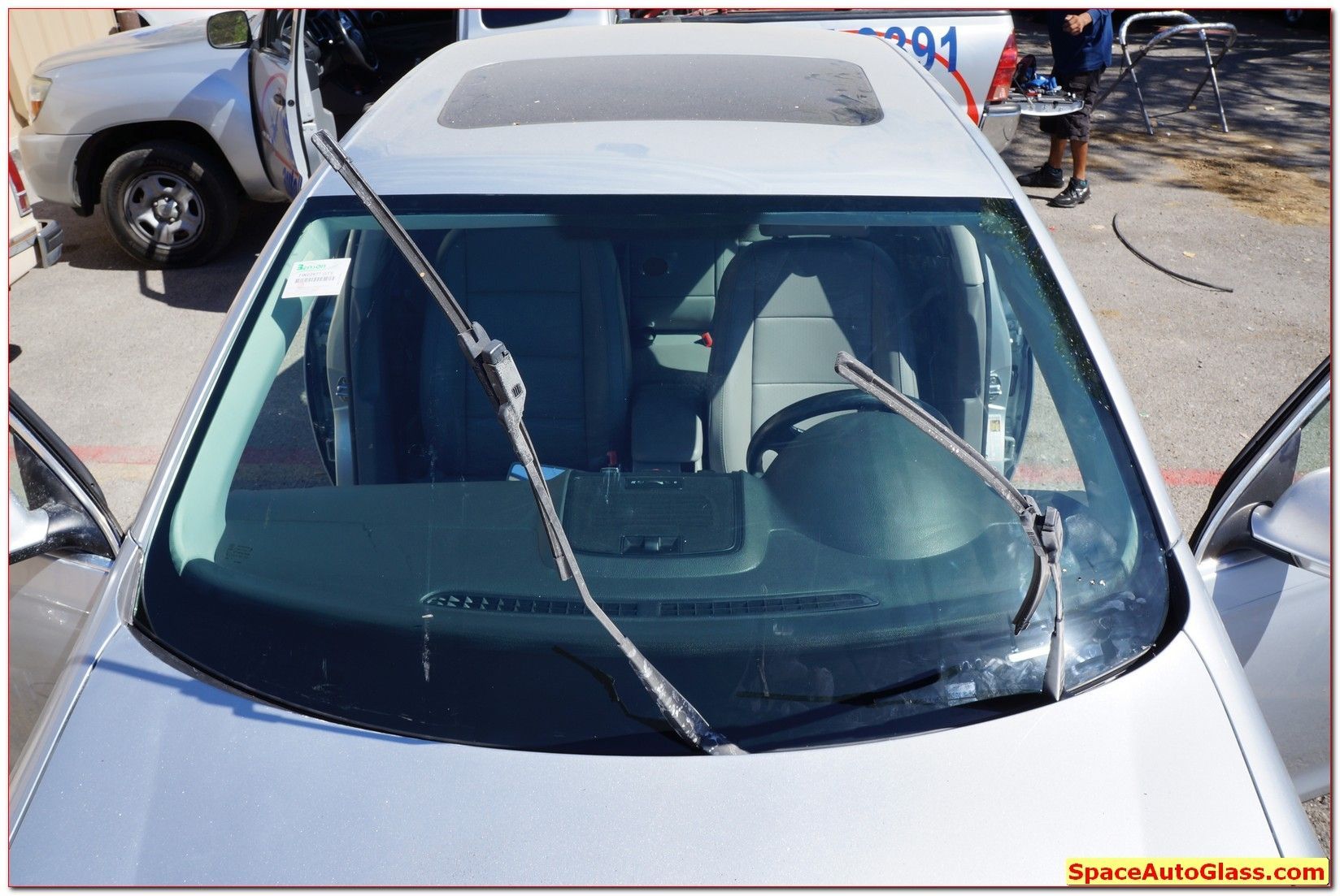Silver car with a cracked windshield and a bent windshield wiper on the hood.
