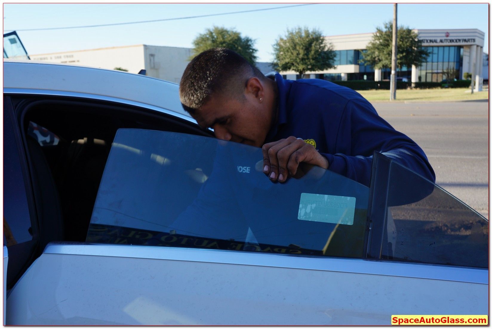 Person leaning into a white car window in a parking lot, looking inside.