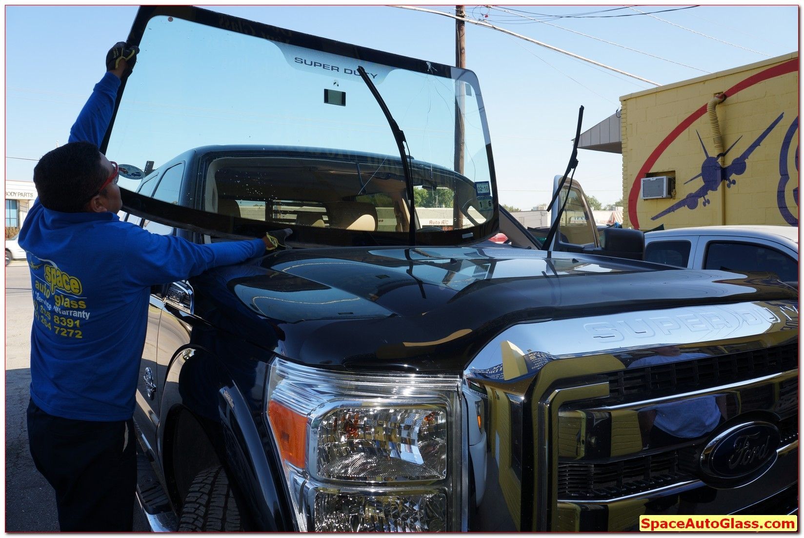 Worker using a crane to load a black pickup truck onto a transport vehicle
