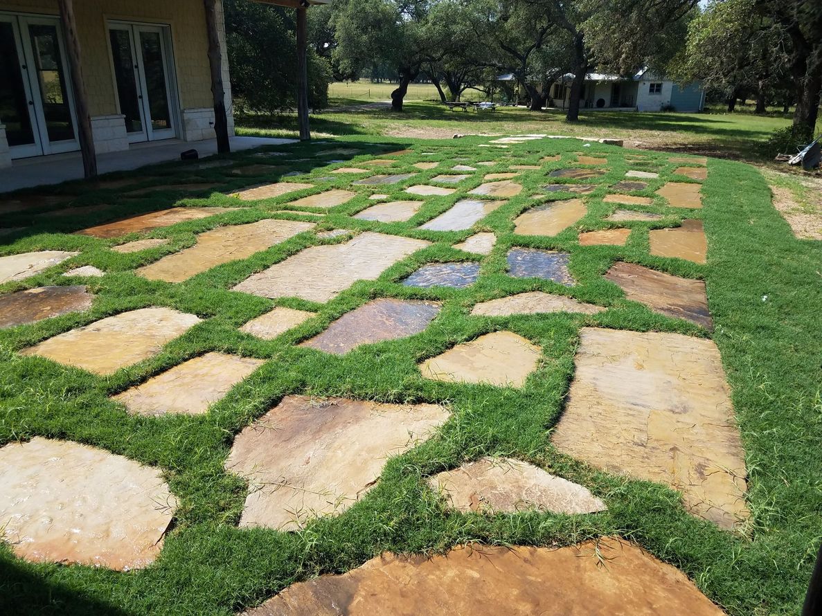 Stepping-stone garden path of irregular tan pavers set in green grass beside a house