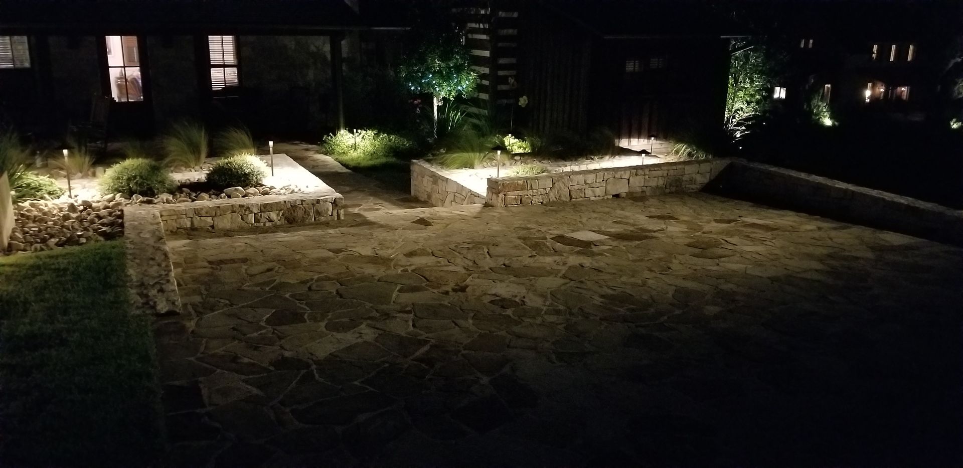 Dimly lit stone courtyard at night with raised planters and small lights along the edges
