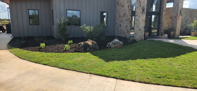 Front yard with green lawn, landscaping rocks, and a modern house exterior beside a driveway