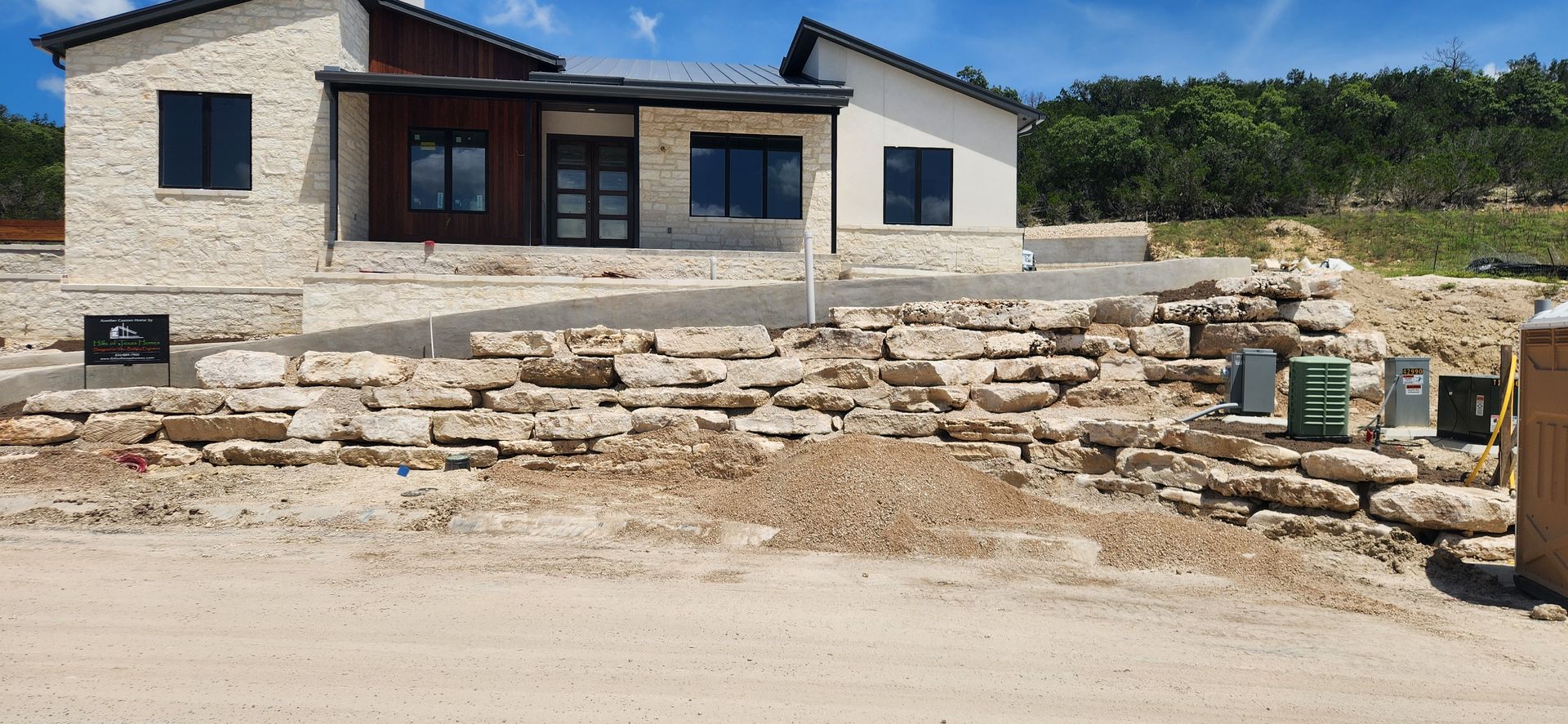 Stone house under construction with a dirt road, stacked rocks, and tools in the foreground