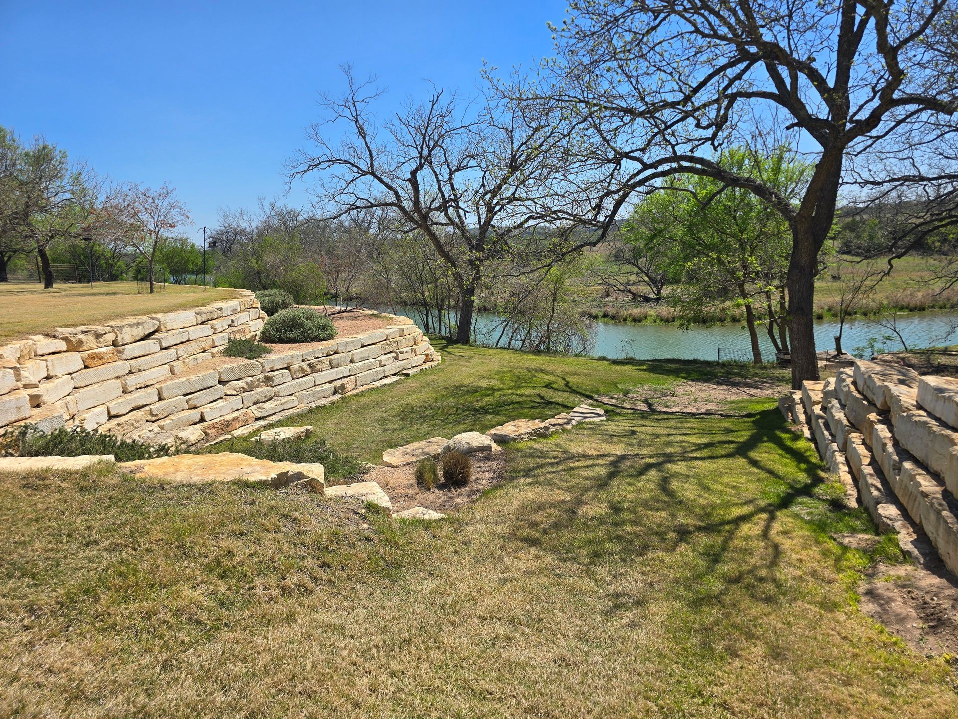 Stone-lined pond in a grassy park with leafless trees and blue sky