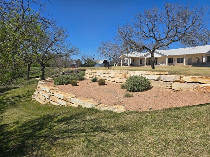 Stone terraced landscape with shrubs and trees in front of a ranch-style house under a blue sky