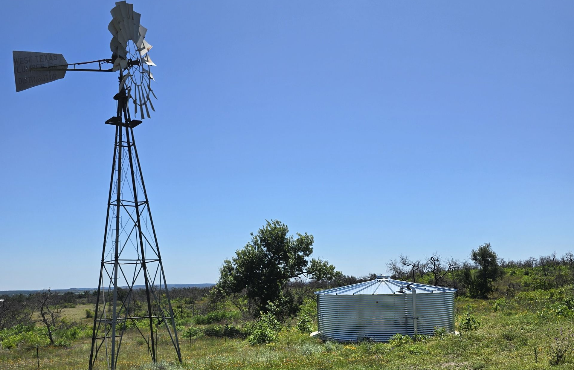 Windmill beside a round water tank in a grassy rural field under a clear blue sky