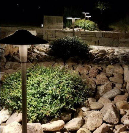 Lit garden with low path lights, rocks, and shrubs at night