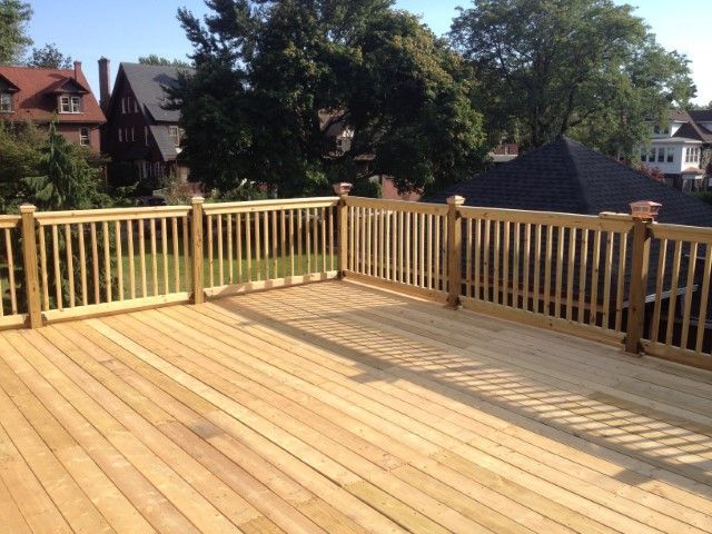Wooden rooftop deck with railing overlooking trees and nearby houses