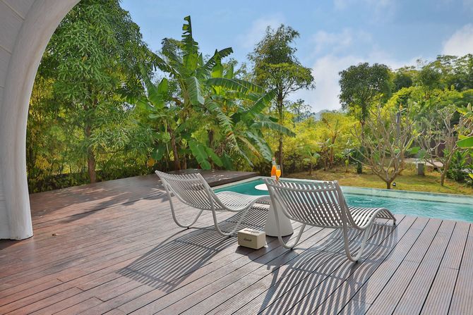 Patio deck with lounge chairs beside a pool, surrounded by lush tropical greenery