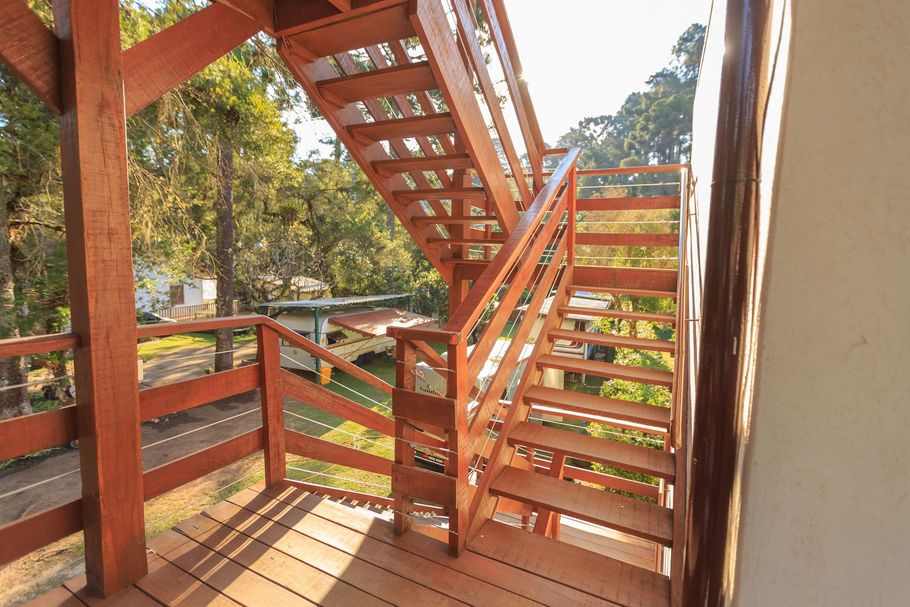 Wooden outdoor staircase with railings on a sunny balcony surrounded by trees