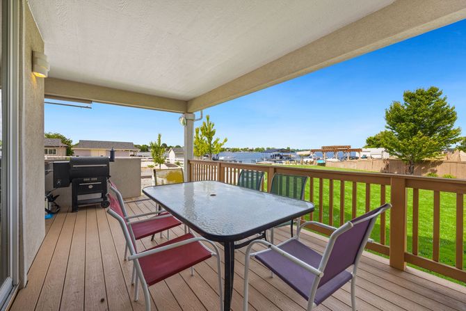 Covered patio with outdoor dining table, chairs, and grill overlooking a green lawn and waterfront.